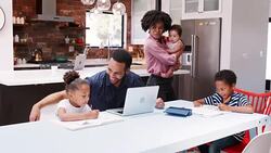 Father helps children with homework whilst mother holds baby daughter in kitchen at home - shot in slow motion Stock Footage