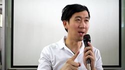 Portrait of young handsome Asian male speaker publicly speaking on stage to group of audience with white board behind Stock Footage
