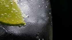 Macro close-up,refreshing soda tonic fizzy water, lime in Glass, ice. Slice of lemon, mineral bubbles. Detox or thirst concept. Healthy, dietary nutrition. Cold lemonade mojito drink. Black background Stock Footage