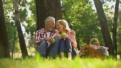 Joyful healthy old couple relaxing on grass, holding apples and hugging, picnic Stock Footage