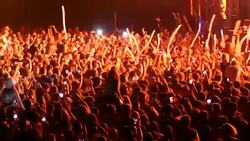 People in the stadium in front of the stage. Spotlights illuminate people in the stadium. Thousands of people in the stadium listen to music and dance. Rays of light from the stage. Many people dance under the stage. Stock Footage