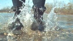CLOSE UP Cheerful girl stomping her feet in the shallow lake and splashing water Stock Footage