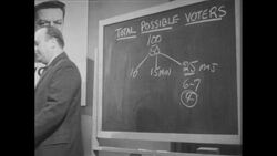 1960s: Man stands at chalkboard, talks, sets chalk down, walks to front of room, talks Stock Footage