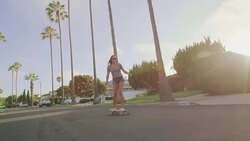 Attractive adventurous girl skateboarding down palm tree lined street at sunset Stock Footage