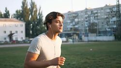 Young fit mixed race man listening to music and working out by running on urban stadium track Stock Footage