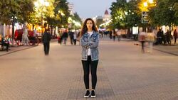 Time-lapse of attractive woman with long curly hair standing in the street with crossed arms and looking at camera on autumn evening when people are moving around. Stock Footage