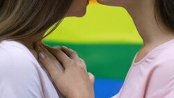 Attractive lesbian couple hugging on rainbow flag background, lgbt, close-up Stock Footage