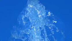A splash of clear ice water. Closeup of light splashing water in sunny fountain in park in summer on blue sky background. Water flow of fountain fly up in air with many splashes. Slow motion. Stock Footage