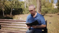 An elderly man with glasses reading an e-book on a Park bench Stock Footage