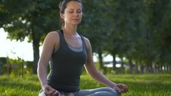 Beautiful slender woman in lotus position practicing yoga in the park Stock Footage