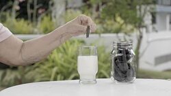 elderly hand dipping and stir a chocolate cookie In milk glass Stock Footage