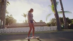 Attractive adventurous girl skateboarding down palm tree lined street at sunset Stock Footage