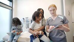 Female nurse showing digital tablet to mother and daughter patient in clinic exam room Stock Footage