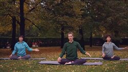 Female yoga instructor is showing stretching exercises then relaxing in lotus position with closed eyes sitting on mats during open-air practice in park. Stock Footage
