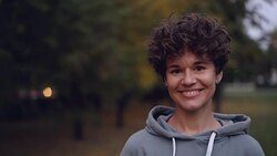 Portrait of good-looking girl with short curly hair looking at camera and smiling then laughing standing outdoors in autumn in city park. People and nature concept. Stock Footage
