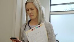 Female doctor with medical chart texting with smart phone in clinic doorway Stock Footage