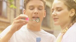 Teen boy blowing soap bubbles, joking and flirting with girlfriend, happy time Stock Footage