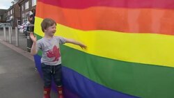 Child standing next to a rainbow flag in support of LGBT school program News Clip