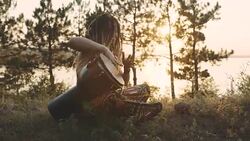 Beautiful young hippie woman with dreadlocks playing on djembe. Funky woman drumming in nature on an ethnic drum at sunset or sunrise with a human skull Stock Footage