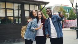 Happy African American guy is taking selfie with friends beautiful Caucasian girls standing in street posing and holding smartphone during journey in foreign country. Stock Footage