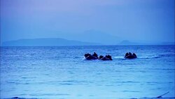 WIDE ANGLE OF SOLDIERS ON THREE SMALL RAFTS OR BOATS PADDLING TO SHORE. OCEAN OR OTHER LARGE BODY OF WATER. MOUNTAINS IN BACKGROUND. SOLDIERS REACH SANDY BEACH AND RUN WITH THEIR MACHINE GUNS. COULD BE DUSK. ARMY. Stock Footage