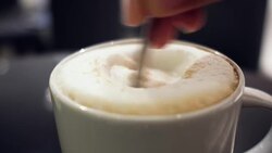 close up hand holding spoon stirring milk foam of cappucino coffee on white cup Stock Footage