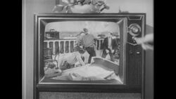 1960s: Man gets up from chair, looks at woman on couch, walks to TV, turns TV knob Stock Footage