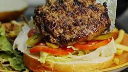 Large hamburger placed on a bun with vegetables in slow motion Stock Footage