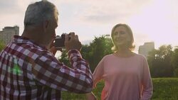 Male pensioner taking picture of attractive senior woman in park, hobby, date Stock Footage