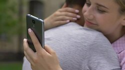 Girl texting on smartphone while embracing boyfriend, lie and betrayal, closeup Stock Footage