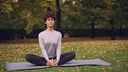 Pretty brunette is stretching legs in Cobbler's pose sitting on yoga mat then bending forward relaxing back and closing her eyes. Relaxation and yoga concept. Stock Footage