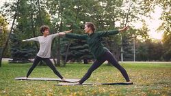 Experienced instructor slender girl is teaching her female student hatha yoga asanas on warm autumn day in city park. Healthy lifestyle and sports for urban people concept. Stock Footage