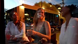 Multi ethnic beautiful group of friends enjoying sweet pastry and drinks at a bakery while talking and laughing Stock Footage