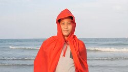 Asian preteen boy in red cover standing on the beach with superhero concept, slow motion. Stock Footage