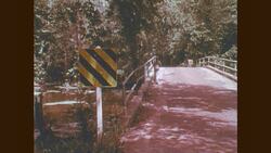1970s: Girl walks along side of road, over bridge Stock Footage