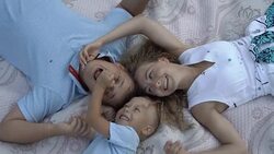 Dad, mom and little son lie on a blanket in the Park head to head, have fun and play. The son laughs and grabs daddy's nose. The view from the top. Stock Footage