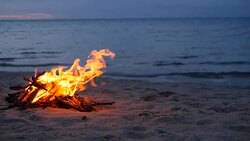 Blazing campfire on the beach during summer evening. Bonfire in nature as background. Burning wood on white sand shore at sunset. selective focus. tropical romantic landscape near sea water edge. Stock Footage