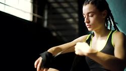 Closeup young beautiful woman sitting on floor and wrapping hands with black boxing wraps in club. Stock Footage