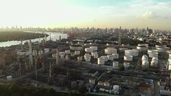 Aerial view over oil refinery factory or chemical plant standing next to big river with Bangkok city in background in evening. Stock Footage