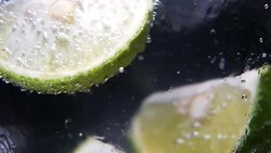 Macro close-up,refreshing soda tonic fizzy water, lime in Glass, ice. Slice of lemon, mineral bubbles. Detox or thirst concept. Healthy, dietary nutrition. Cold lemonade mojito drink. Black background Stock Footage