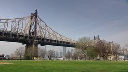 WIDE ANGLE OF QUEENSBORO BRIDGE OVER EAST RIVER. SEE TREES AND GRASS IN PARK AREA. COULD BE PLAYING OR GAME FIELD. SEE NEW YORK CITY SKYLINE WITH SKYSCRAPERS AND TALL OFFICE BUILDINGS IN BACKGROUND. QUEENS. Stock Footage