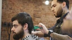 Young barber trimming customer's hair in salon Stock Footage