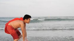 Happy fat boy in red hood splashing water on the beach, slow motion Stock Footage