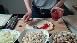 Young woman spreading tomato sauce on pizza dough Stock Footage