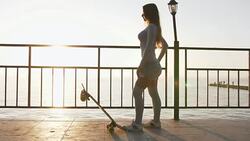 Beautiful and fashion young woman posing with a skateboard during sunrise at seafront, slow motion, dolly shot Stock Footage