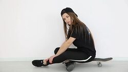 teenage girl in trendy hip hop clothes and cap posing against white wall with skateboard Stock Footage