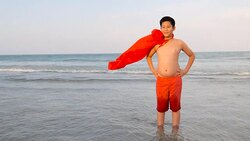 Asian preteen boy in red cover standing on the beach with superhero concept, slow motion. Stock Footage