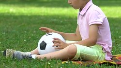 Lonely boy sitting in park with ball, no friends to play with, bullying problem Stock Footage
