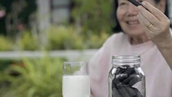 elderly hand dipping and stir a chocolate cookie In milk glass Stock Footage