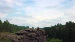 A sniper with a rifle sits on top of the mountain and inspects the territory. View from the drone. the camera moves from the soldier, revealing a view of the landscape Stock Footage